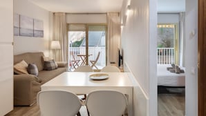 A modern living room with a sofa, dining table, chairs, and a balcony with a view.