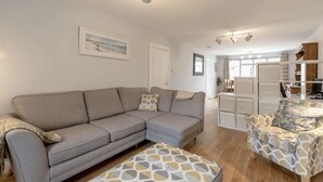 A living room with a grey sofa, patterned ottoman, and a white cabinet with drawers.