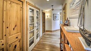 Un corridoio con pavimento in legno, una porta in legno, una porta in vetro e una scrivania con un quadro incorniciato e un libro.