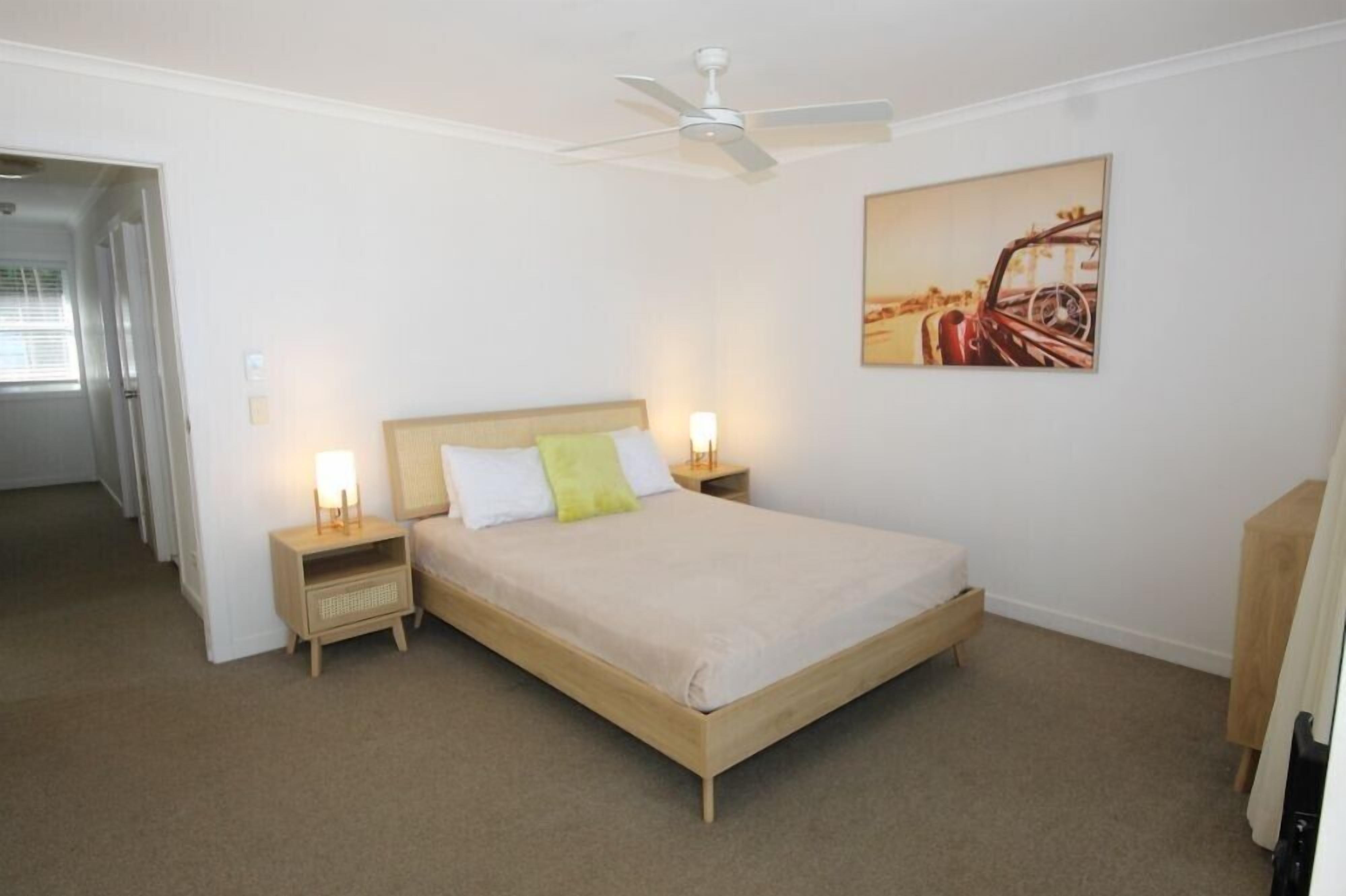 Ein Schlafzimmer mit einem Einzelbett, zwei Nachttischen, einem Deckenventilator und einem an der Wand hängenden Gemälde.