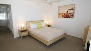A bedroom with a single bed, two bedside tables, a ceiling fan, and a wall-mounted painting.