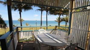 A covered outdoor area with a table and chairs, overlooking a beach with palm trees and the ocean.