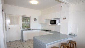 A modern kitchen with white cabinets, a grey countertop, a microwave, and three wooden stools.