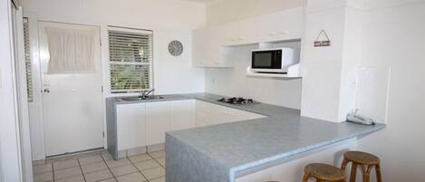 Una cocina moderna con armarios blancos, una encimera gris, un microondas y tres taburetes de madera.
