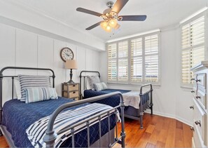 Un dormitorio con dos camas, un ventilador de techo, un reloj y una ventana con persianas.