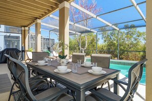An outdoor patio with a table set for dining, surrounded by chairs, and overlooking a swimming pool. - 5 bed/4 Bath Home with Pool/ Spa/ Games Room - Nr Champions Gate  (Davenport)