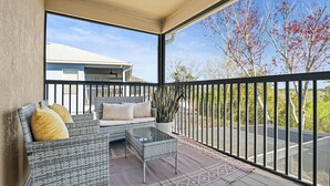 Ein Balkon mit Korbmöbeln, einem Glastisch und einem Blumentopf.