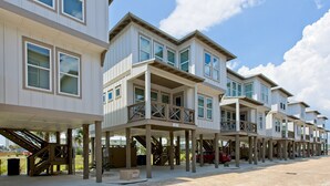 A row of multi-story beachfront homes with balconies and a covered walkway. - Coastal chic beach home in Cottages at Lagoon Pass with EV charger and pool. (Gulf Shores)