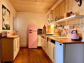 Une cuisine avec des meubles de rangement en bois, un réfrigérateur rose et un lave-vaisselle blanc.