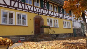 A traditional half-timbered building with a yellow facade, a wooden door, and a staircase leading to the entrance. - Kanne Cottage Flaire Suite with Stream and Meadow (Epfendorf/Trichtingen)