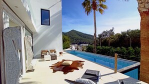 Ein Poolbereich mit Blick auf einen Berg, eine Palme und ein weißes Gebäude mit einem Fenster.