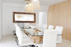 Een moderne eethoek met een glazen tafel, witte stoelen, een houten detail en een grote spiegel.