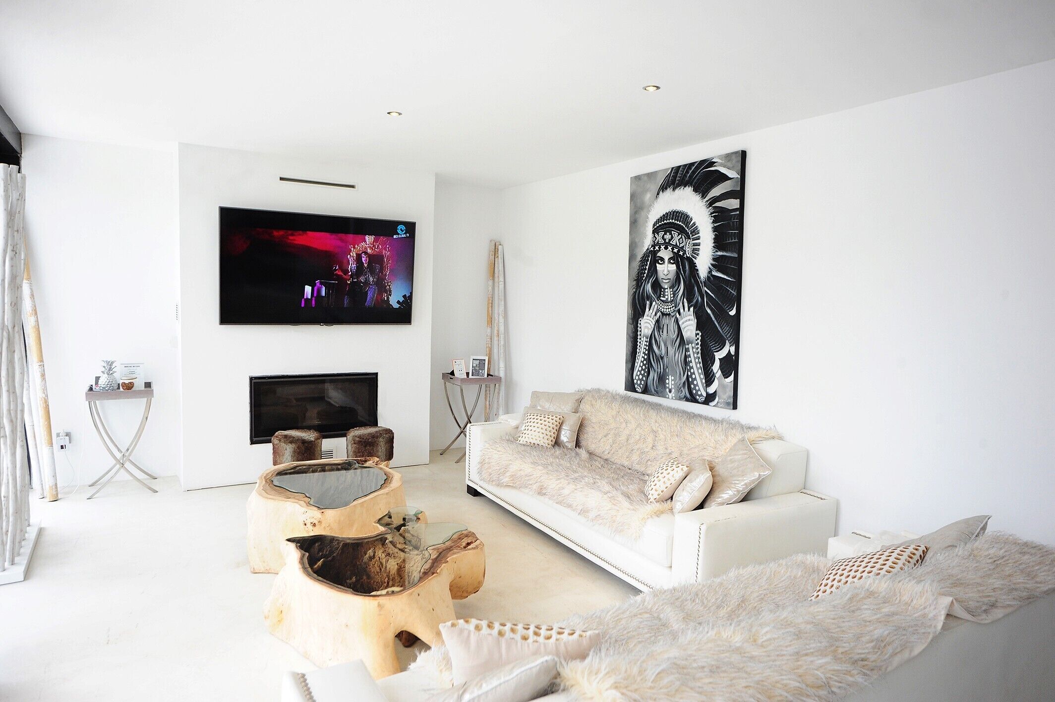 A modern living room with a white sofa, a flat-screen TV, a large abstract painting, and a unique wooden coffee table.
