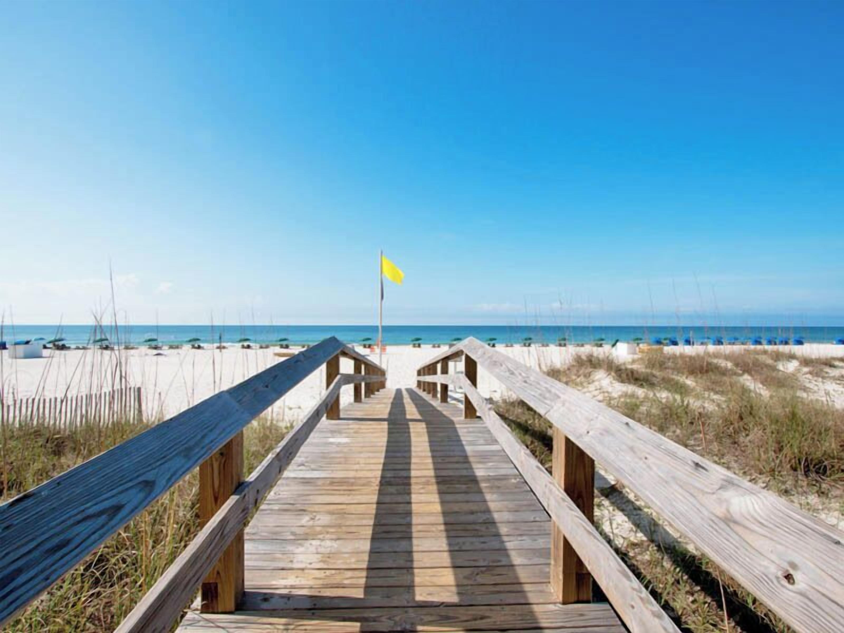 A wooden boardwalk leading to a beach with a yellow flag marking the path.