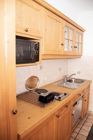 A kitchen with wooden cabinets, a microwave, a sink, and a stove. - Winklmoosalm Vacation Rental (Reit im Winkl)