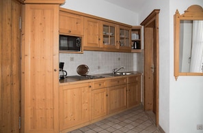 A kitchen with wooden cabinets, a microwave, a kettle, and a sink.