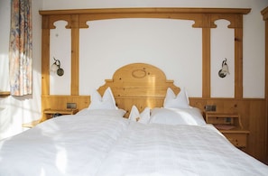 A hotel room with a wooden headboard, white bedding, two bedside tables with lamps, and a window with curtains. - Panorama Vacation Apartment in a Central Location (Reit im Winkl)