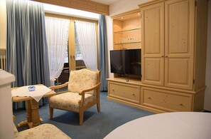 A hotel room with a wooden chair, a television on a wooden cabinet, and a table with a glass on it. - Enzian Apartment in a Central Location (Reit im Winkl)