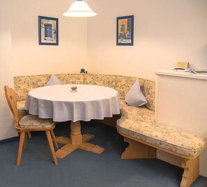 A corner dining area with a round table, two chairs, a bench, and two framed artworks on the wall. - Enzian Apartment in a Central Location (Reit im Winkl)