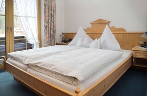 A double bed with a wooden headboard, a bedside table with a lamp, and a window with curtains. - Enzian Apartment in a Central Location (Reit im Winkl)