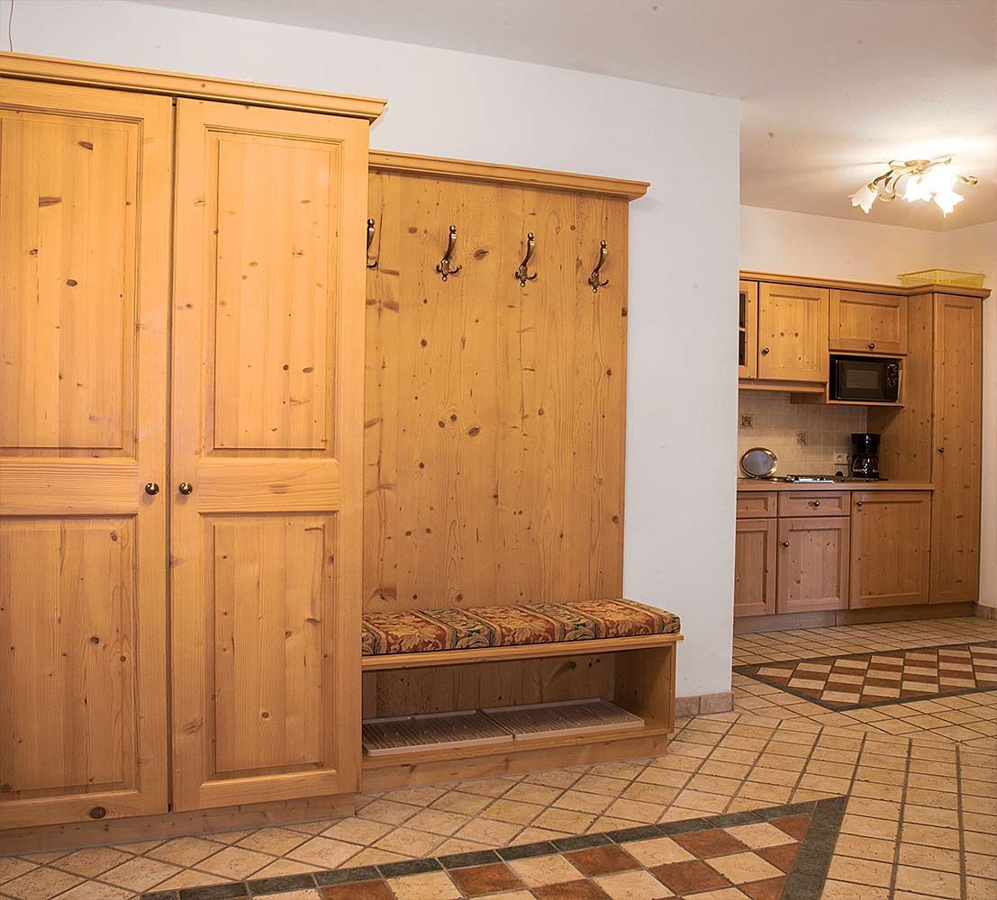 A room with wooden cabinets, a bench, and a kitchen area with a microwave.