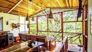 Un interior rústico de madera con comedor, cocina y ventanas amplias que ofrecen vistas del exterior.