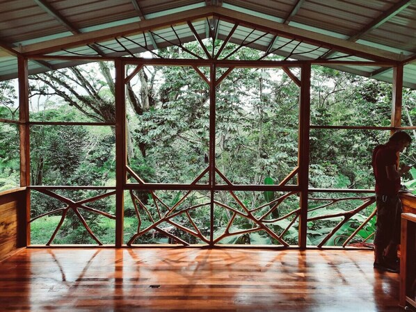 A wooden deck with a metal framework and glass panels, overlooking a dense forest.