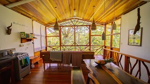 Un interior rústico de madera con cocina, bancos de madera y ventanas amplias que ofrecen vistas a la vegetación.