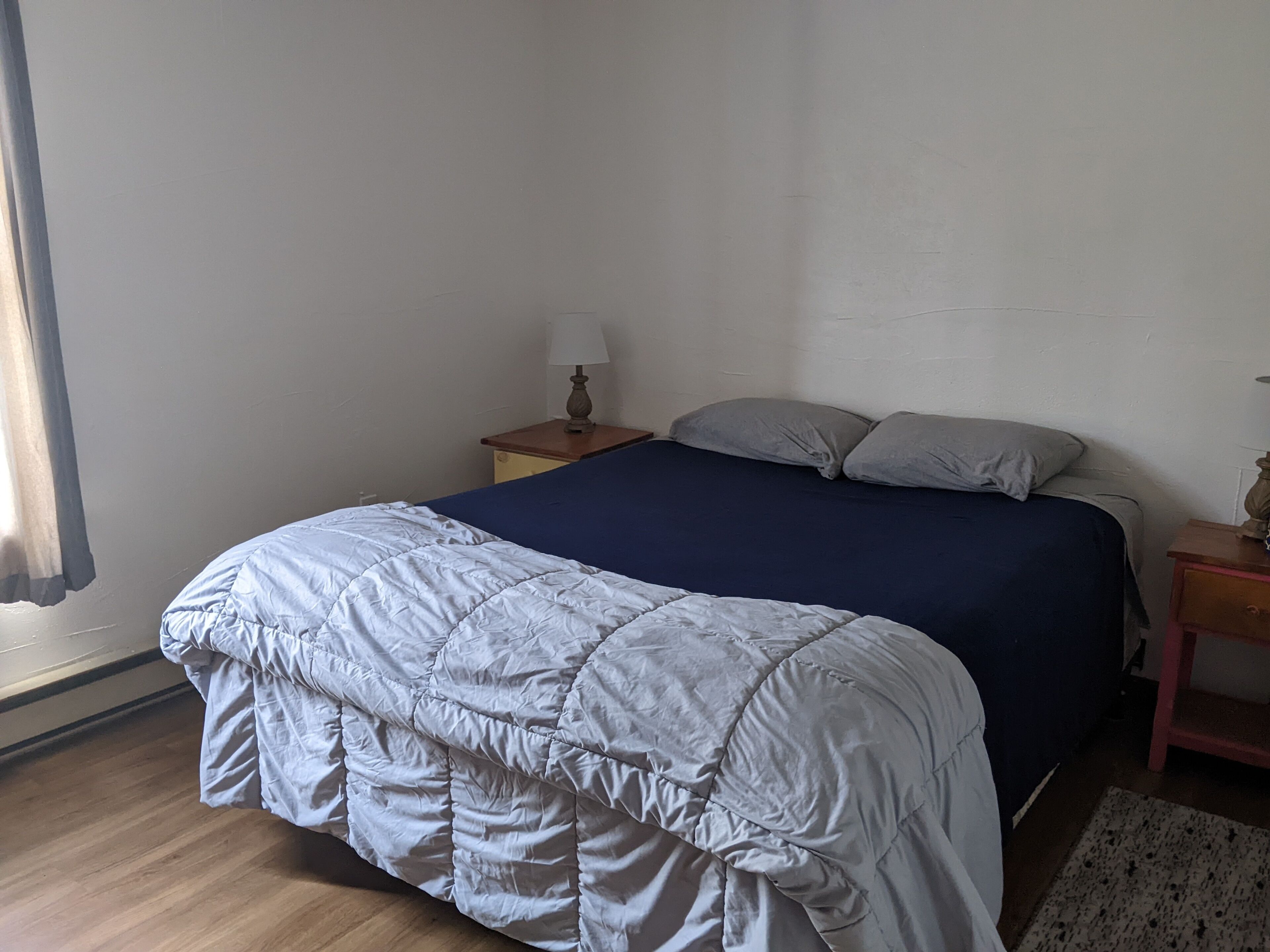 Una camera da letto con un letto, un comodino, una lampada e una finestra con tende.