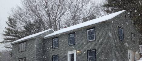 A two-story house with a snow-covered roof and windows, surrounded by trees.