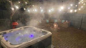 A hot tub with steam, surrounded by a brick patio and string lights.