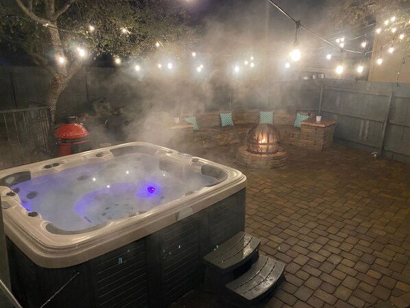 Un bain à remous avec jets de vapeur, entouré d’une terrasse en briques et illuminé de guirlandes lumineuses.