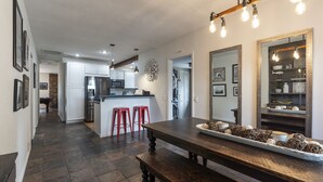 A modern kitchen with white cabinets, a central island, red bar stools, and a dining table with a decorative centerpiece.