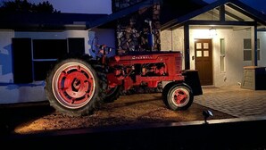 A red Farmall tractor parked in front of a house with a stone chimney and a garage.