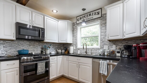 A modern kitchen with white cabinets, a stainless steel microwave, an oven, and a sink.