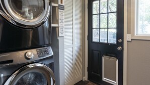 A laundry room with two stacked front-loading washers and dryers, a door with a window, and a light fixture above.