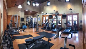 A gym with various exercise equipment, wooden floors, and large windows.