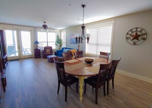 A dining area with a wooden table and chairs, a ceiling fan, and a large window with blinds.