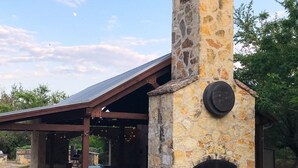 A stone-built outdoor kitchen area with a chimney, surrounded by outdoor seating and greenery.