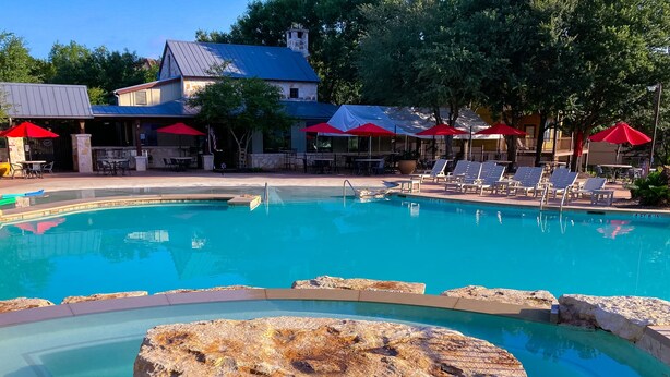 A pool with a large rock in the center, surrounded by lounge chairs and umbrellas.