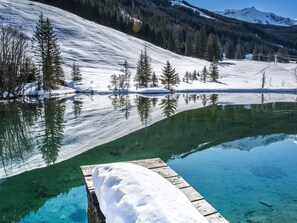 Una vista despejada de un lago con un muelle de madera y suelo cubierto de nieve.