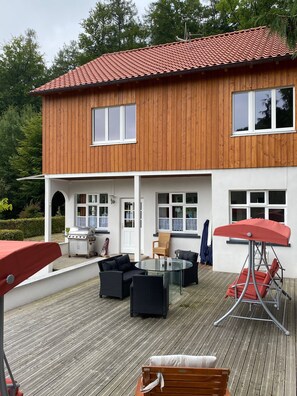 Ein zweistöckiges Holzhaus mit Balkon, Sitzbereich im Freien und einer Hängeschaukel.
