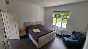 Ein Schlafzimmer mit Bett, Stuhl, Fenster und Tür.
