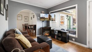 A living room with a fireplace, a dining area, and a view of the outside. - Historic Drake Cottage 30 Day Rental. Across from Drake Park, Mirror Pond, downtown Bend. Furnished. (Bend)