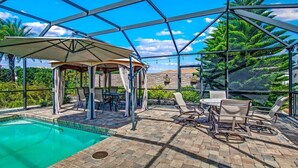 A covered outdoor pool area with a gazebo, lounge chairs, and a table. - Private Corner Oasis with Heated Saltwater Pool (Palm Coast)