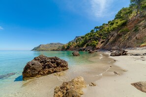 Una spiaggia con acque limpide, rocce e montagne sullo sfondo.