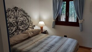 Quarto com cama, mesa de cabeceira, luminária, janela com cortinas e um quadro na parede.