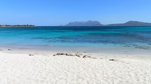 Une plage à l’eau turquoise et limpide, au sable blanc, bordée de formations rocheuses lointaines.
