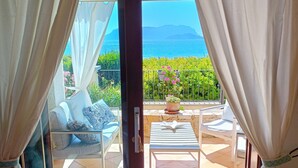 Quarto com vista para o mar, varanda com cadeira e mesa, e cortinas.