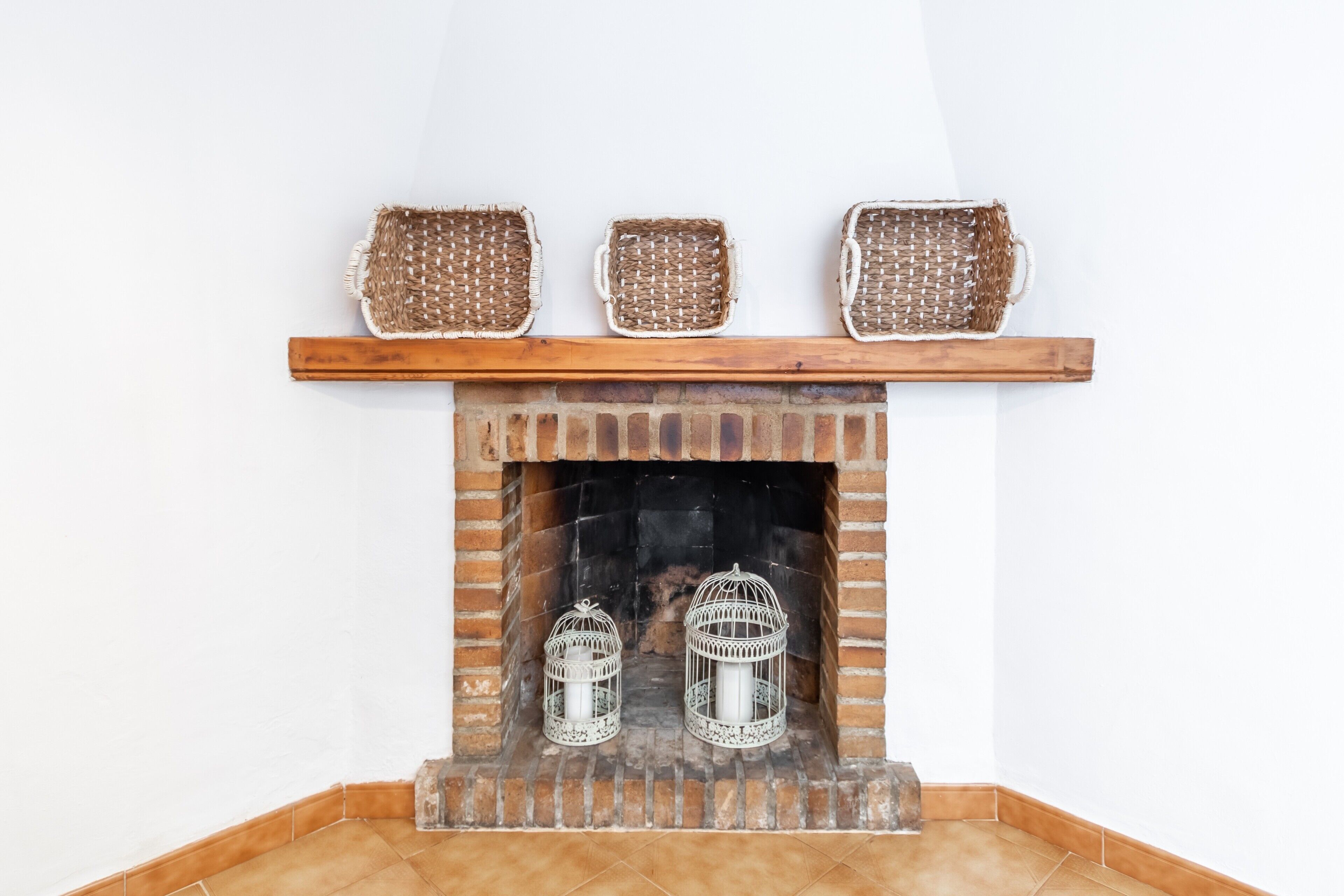 A fireplace with three woven baskets on the mantel, two white candle holders, and a brick surround.